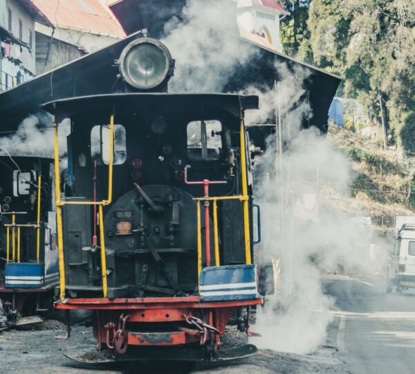 The iconic Darjeeling Himalayan Railway steam engine passing through hills.