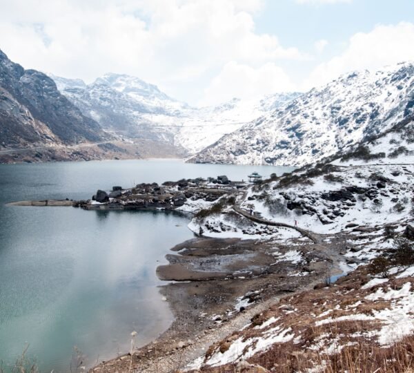 Crystal-clear glacial waters of Tsomgo Lake surrounded by snow-capped peaks.